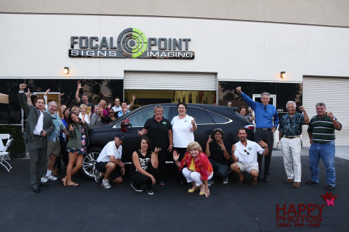 Focal Point Signs & Imaging in Costa Mesa celebrates with friends and family with a Grand Opening photo taken under their exterior business sign surrounding a car wrap they did in Matte Black